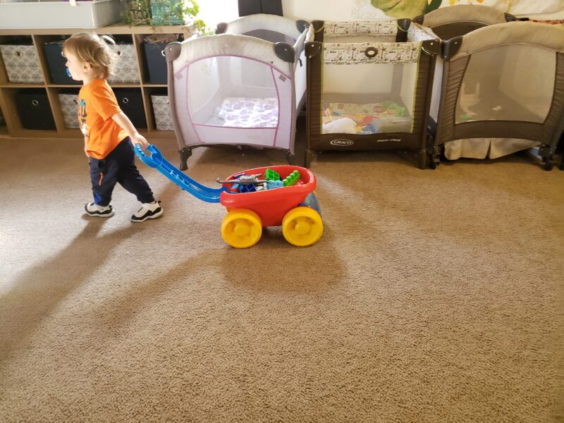 A child pulling a toy wagon in the playroom